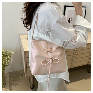 Chic pink bucket bag detail with bow decoration worn by a model in a cozy indoor setting