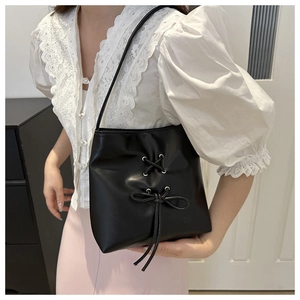 Close-up of elegant black bow-knot bucket bag carried by a model with lace shirt
