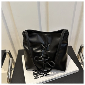 Detail of black leather tote bag featuring a decorative bow and silver eyelets on a stand