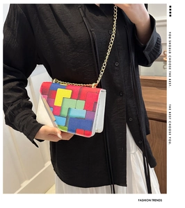 Detail of color-block flap bag with geometric puzzle patterns and gold metal bar strap