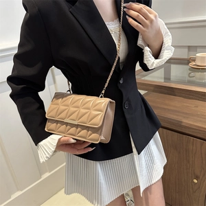Sac à bandoulière beige matelassé avec chaîne dorée porté sur un blazer noir