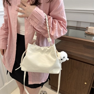 White drawstring bucket bag with woven handle and plush charm shown on model