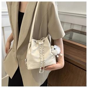 Detail of off-white bucket bag with drawstring closure and plush puppy charm accessory