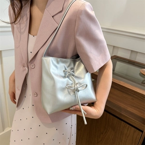 Silver metallic shoulder bag with bow detail held by model in soft indoor lighting