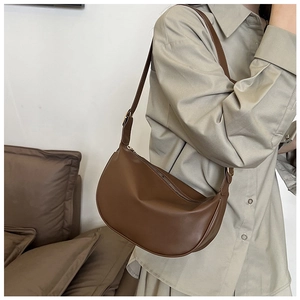 Brown faux leather half-moon shoulder bag shown on model with adjustable strap and gold hardware