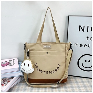 Dettaglio borsa shopper beige con base marrone, tracolla e ciondolo con sorriso
