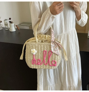 Detail of woven straw bag featuring pink hello embroidery and floral scarf handle