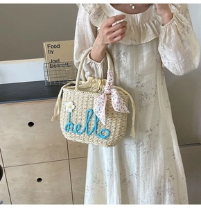 Detail of hand-woven straw bag with hello embroidery and floral scarf on handle
