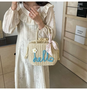 Detail of woven straw handbag with 'hello' embroidery and daisy charm accessory