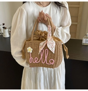 Detail of straw woven handbag with hello embroidery and pink floral scarf decoration