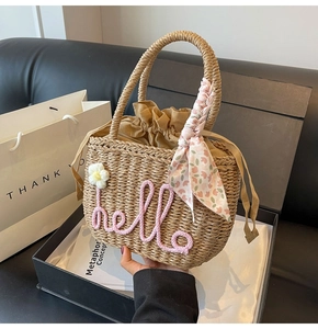 Detail of woven straw bag with hello embroidery and decorative floral silk handle scarf