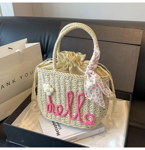 Detail of woven straw tote with pink hello embroidery and floral scarf in a gift box