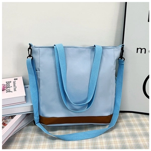 Dettaglio borsa tote in tela azzurra con fondo in pelle marrone e tasca laterale esterna