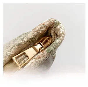 Detailed macro shot of a gold metal zipper and green floral embroidery on a woven bag
