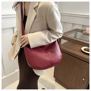 Detail of a dark red leather crescent bag with fine texture on a female model shoulder