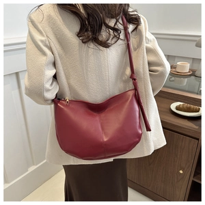 Detail of burgundy leather crescent shoulder bag with stylish knotted strap design