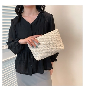 Detail of cream woven handbag with floral embroidery held by a model in black shirt