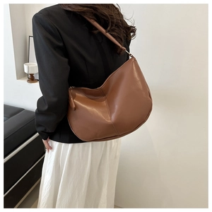 Brown faux leather hobo bag worn on shoulder showing its curved crescent shape and wide strap