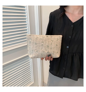 Detail of straw woven clutch featuring green leaves and white flower embroidery with zipper