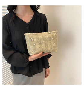 Detail of woven straw handbag featuring white floral embroidery and natural texture