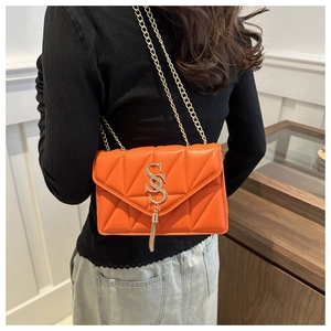 Detailed view of orange quilted PU leather shoulder bag with gold S-logo and fringe