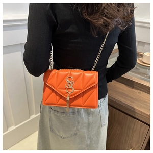 Detail view of orange quilted crossbody bag with gold chain strap and fringe charm on model
