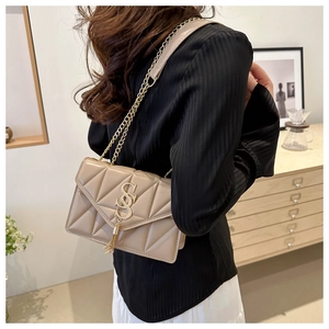 Detail of apricot quilted crossbody bag with gold SS logo and chain strap on shoulder