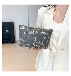 Detail of floral embroidery on a dark grey canvas crossbody bag held by a model