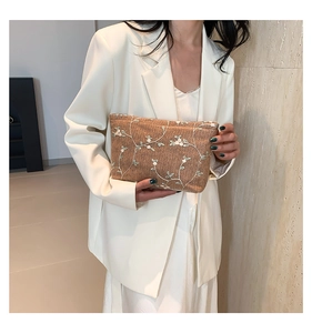 Detail of a brown woven clutch featuring white floral embroidery and zipper closure