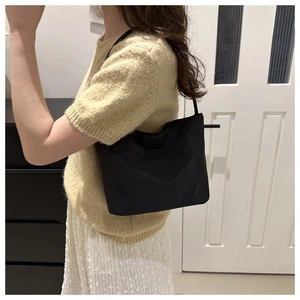 Detail of minimalist black nylon underarm bag with embroidered letters on model