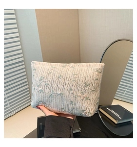 Detailed embroidery of pink flowers and green leaves on cream woven crossbody bag
