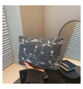 Close-up of elegant floral vine embroidery on a dark grey woven fabric shoulder bag