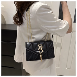 Detail of a black quilted crossbody bag with a gold S buckle and tassel on white satin