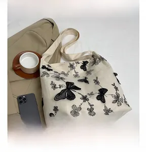 Detail of canvas tote bag featuring black lace butterfly embroidery and floral patterns