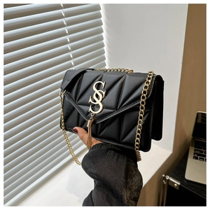 Detail of black quilted crossbody bag featuring gold chain and metallic logo with tassel
