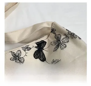 Close-up of intricate black lace butterfly embroidery on a beige canvas tote bag surface