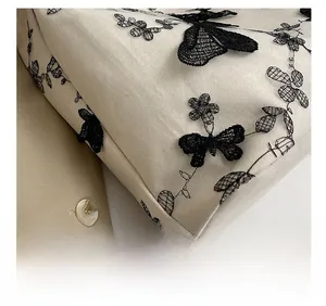 Close-up of precise stitching and black lace butterfly embroidery on beige canvas tote