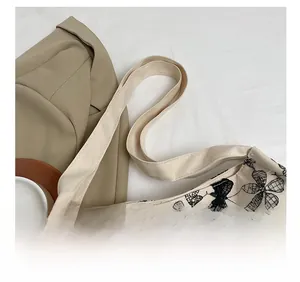 Detail of canvas tote shoulder strap connection and intricate black butterfly embroidery