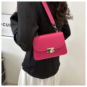 Détail du sac bandoulière magenta avec boucle dorée sur un mannequin en chemise rayée