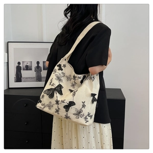 Detail of off-white tote bag featuring 3D black lace butterfly embroidery and canvas texture
