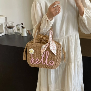 Straw woven handbag with hello lettering and floral ribbon shown in a lifestyle setting