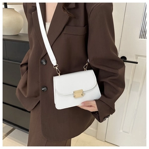 Détail du petit sac blanc avec boucle dorée porté sur un ensemble marron