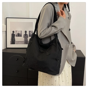 Detailed close-up of 3D butterfly embroidery and lace on a black underarm tote bag