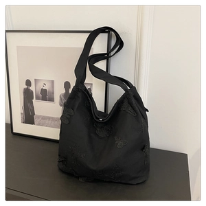Detail of black tote bag featuring delicate butterfly lace embroidery and silver magnetic clasp
