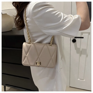Dettaglio della borsa a tracolla beige trapuntata con catena dorata su una modella