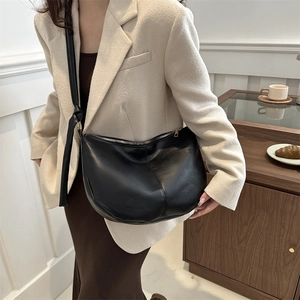 Minimalist black leather half-moon tote bag worn over the shoulder for commute