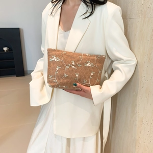 Bohemian woven crossbody bag with floral embroidery held by model in white suit