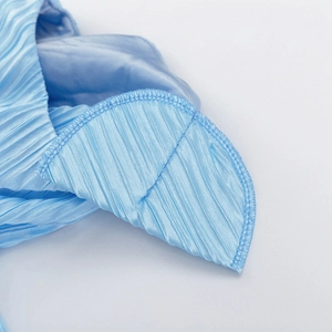 Dettaglio del tessuto plissettato azzurro con cuciture fini e texture lucida dell'abito