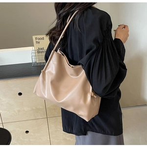 Dettaglio di una borsa tote in pelle beige con nodi laterali e una tracolla sottile