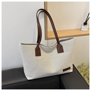 Close-up of a large capacity beige nylon tote bag with brown leather handles and fashion patch